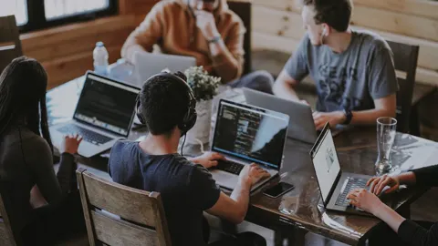 Equipo colaborando alrededor de computadoras y un tablero de trabajo