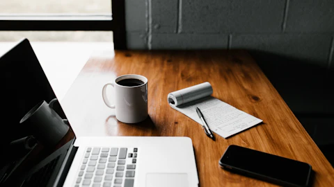 MacBook Pro, una taza blanca y un smartphone sobre la mesa