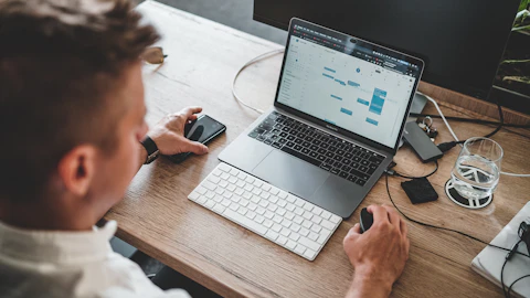 Persona usando el mouse y el iPhone junto a una MacBook Pro